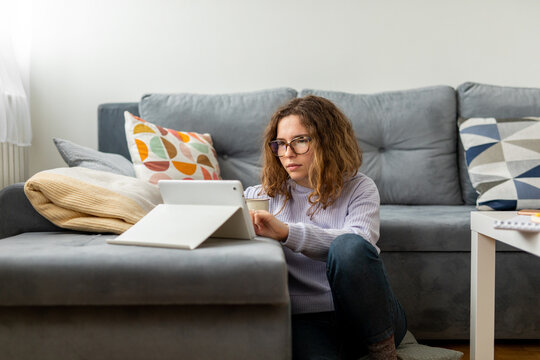 Young woman sitting on the floor next to the  sofa at home and using tablet 