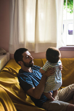 Man holding and talking with his child sitting on the couch at home