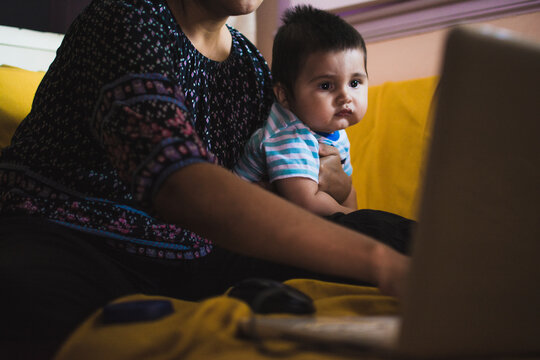 Mother using computer with baby in her arms