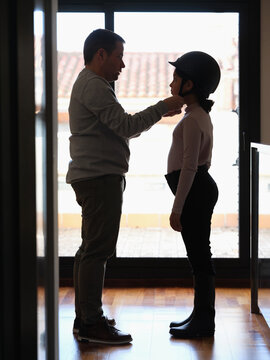 Dad dressing daughter helmet for equitation.