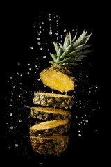 fresh and sliced pineapple with juice splashes on black background