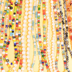 Closeup of necklaces made from multicolored beads and pearls on a golden background.