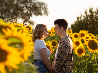 Pareja joven disfrutando de sus vacaciones en un campo de girasoles durante la puesta de sol en...