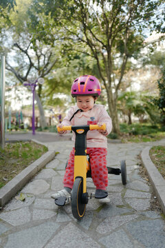 Two year old girl wearing a helmet riding a tricycle