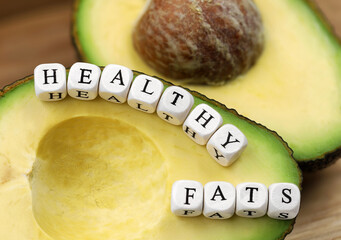 halfed ripe avocado with text from letter cubes, healthy fats concept