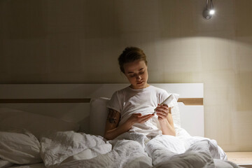 Young woman applying hand cream sitting in bed