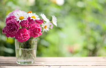 bouquet flowers of pink roses and chamomiles in the glass vase on the nature blurred background with bokeh lights