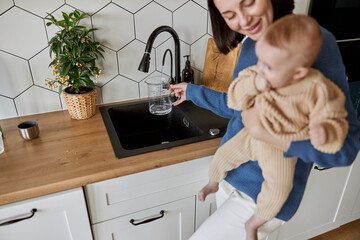 Woman pouring water to glass cup from kitchen sink