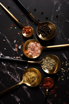 Golden spoons with spices on dark marble