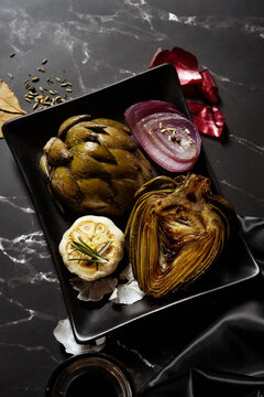 Grilled artichoke with garlic and onion on a dark plate setting