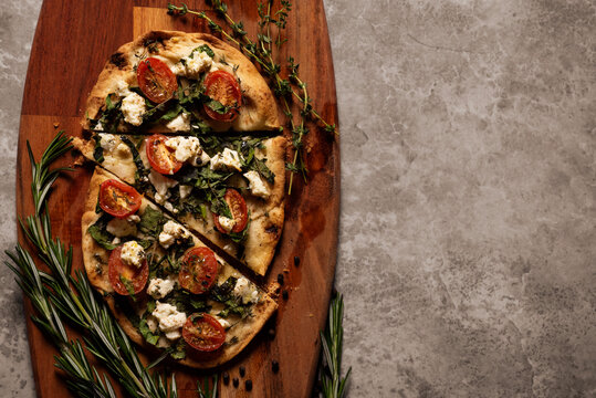 Baked flat bread with vegetables and herbs on a wooden cutting board