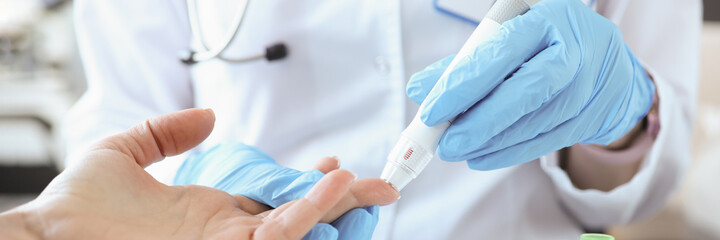Doctor with gloves piercing patients finger with lancet closeup