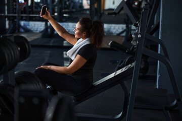 Jolly young woman taking photo in gym