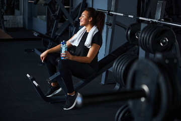 Fototapeta na wymiar Cheerful fit woman drinking water after workout indoors