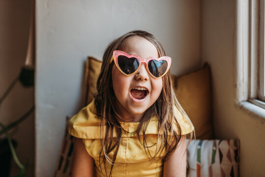 Little girl with pink heart sunglasses and princess dress at home.