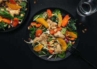 Sesame chicken salad with orange slices on dark background 