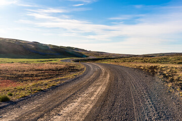 Fototapeta na wymiar Empty winding gravel road in a barren landscape in Iceland on a sunny summer day. Lens flare.