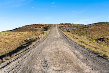Gravel dirt road going up in a barren landscape in the Iceland highlands under blue sky in summer