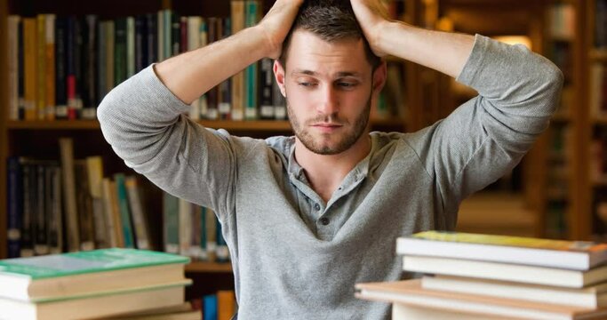 Animation of stressed male mature student with piles of study books, holding head in library