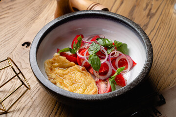 Delicious breakfast with roasted eggs and ripe tomato salad with red onion, side view on rustic wooden table