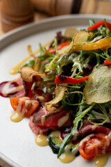 Gourmet restaurant salad with mixed greens, roast beef and potato  chips, wooden table in a restaurant