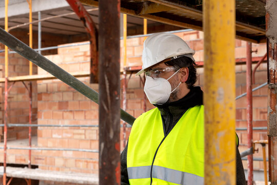 Workman In Hardhat And Protective Mask Working On Construction Site