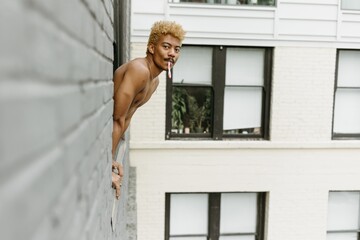 Young man brushing teeth out a window