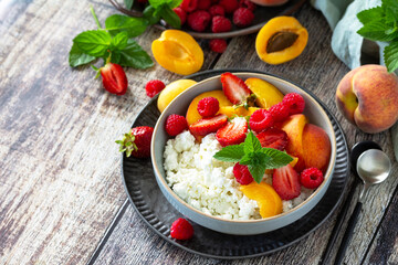 Rustic summer breakfast or dessert. Curd or cottage cheese served with fresh summer fruits and berries on a wooden table. Copy space.