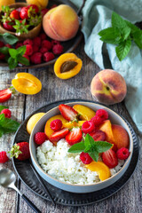 Rustic summer breakfast or dessert. Curd or cottage cheese served with fresh summer fruits and berries on a wooden table.