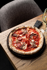 Top view of sausage pizza on a rustic wooden cutting board with a glass of white wine