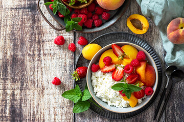 Rustic summer breakfast or dessert. Curd or cottage cheese served with fresh summer fruits and berries on a wooden table. Top view flat lay. Copy space.