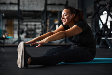 Cheerful young woman exercising flexibility in gym