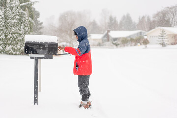 Boy reaches to grab mail from snowy mailbox