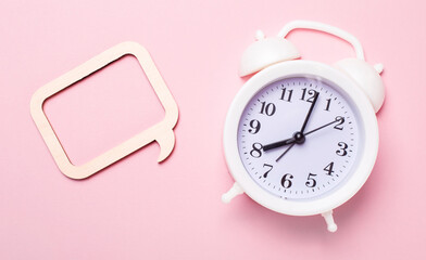 On a delicate pink background, a white alarm clock and a frame with a place to insert text or an...