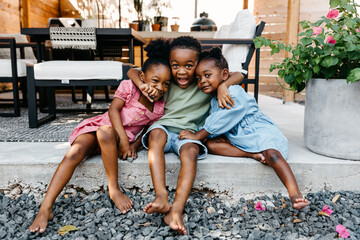 Three kids playing outside in the backyard sitting on the patio. 