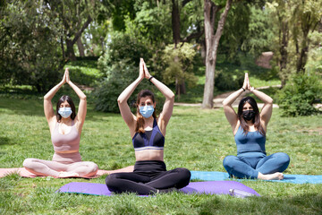 Three Caucasian girls with face mask practicing yoga outdoors. Space for text.