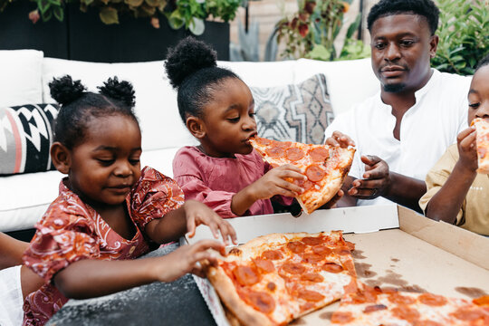 An African American family gathered around a table eating pizza. 