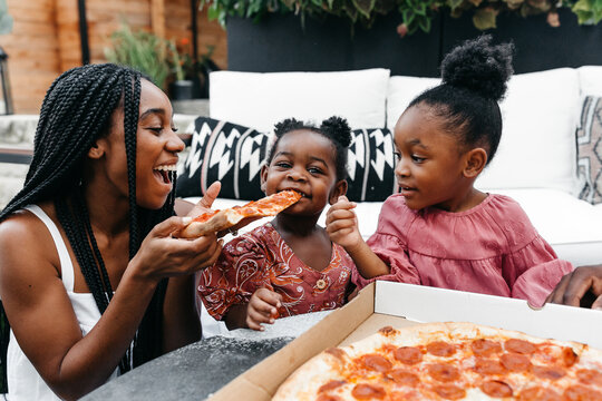 An African American family gathered around a table eating pizza. 