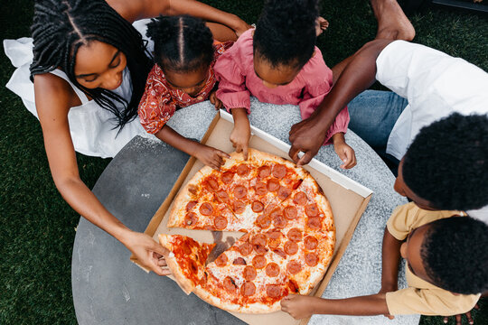 An African American family gathered around a table eating pizza. 