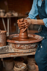 Unrecognized craft woman arms shaping clay pot in pottery workshop