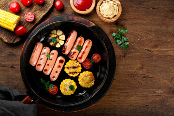  Grilled sausages with vegetables and sauces. Summer BBQ with sausages, corn and tomatoes on the wooden table top view, photo with copy space for text