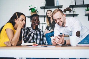 Cheerful diverse colleagues discussing project and using smartphone