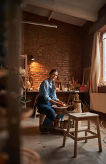 Young Caucasian ceramicist shaping clay pot in pottery workshop