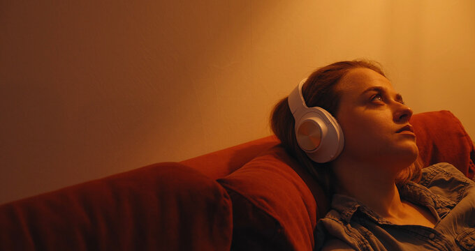 Depressed young woman listening to music on sofa