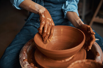 Beautiful elegant female artisan hands shaping clay tableware in pottery workshop