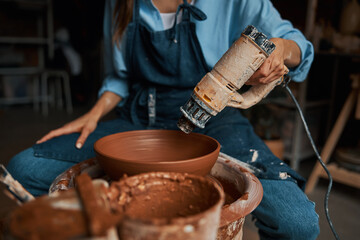 Focused charming craft woman holding blowtorch in hand in pottery workshop