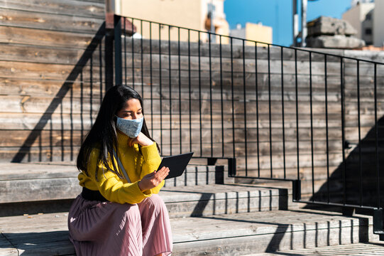 Woman in mask reading electronic book in city
