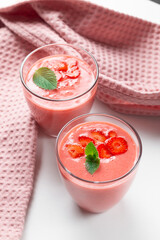 Fresh strawberry milkshake decorated with berries and mint on a light background in pastel colors, space for text, the concept of a healthy breakfast, diet and good nutrition.