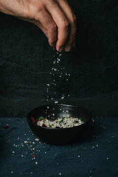 Hand sprinkling salt over a ceramic bowl