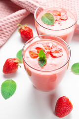 Fresh strawberry milkshake decorated with berries and mint on a light background in pastel colors, space for text, the concept of a healthy breakfast, diet and good nutrition.